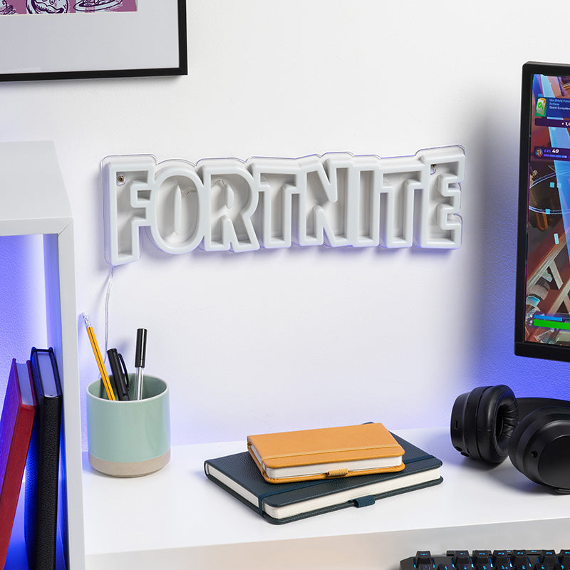 Desk setup with 'Fortnite' sign, notebook, pens, and computer monitor.
