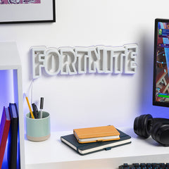 Desk setup with 'Fortnite' sign, notebook, pens, and computer monitor.